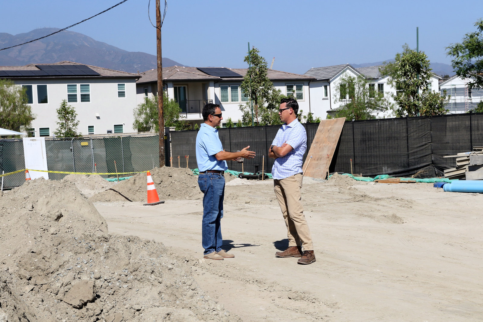Two men talking on a graded construction site in front of new homes