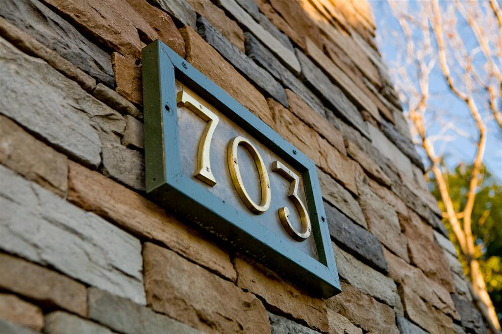 Brass building number 703 on a framed plaque set in a stacked-stone wall